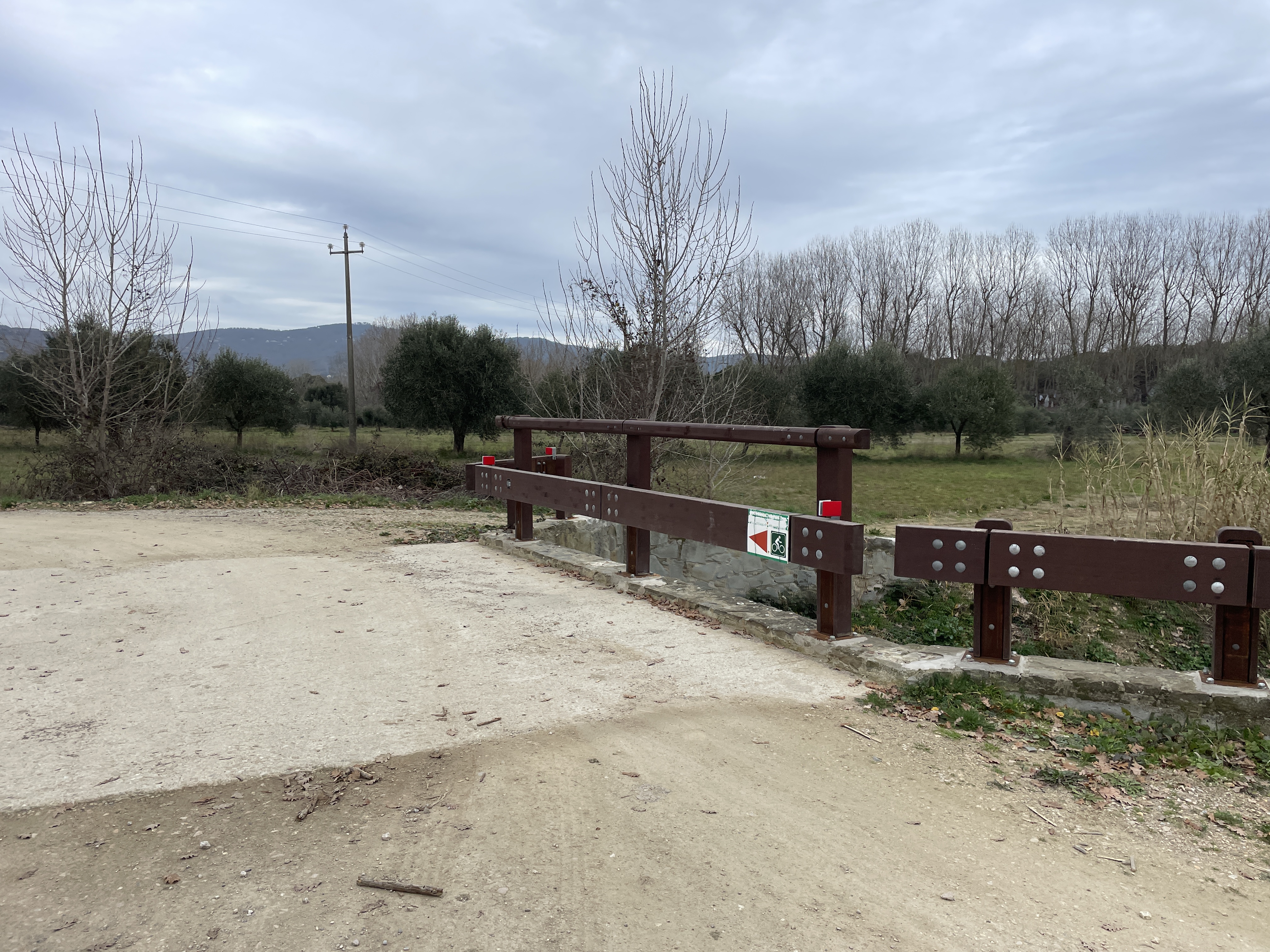 Brown barrier bounds a concrete bridge over the cycle path. Green and white sign indicates direction to cyclists.